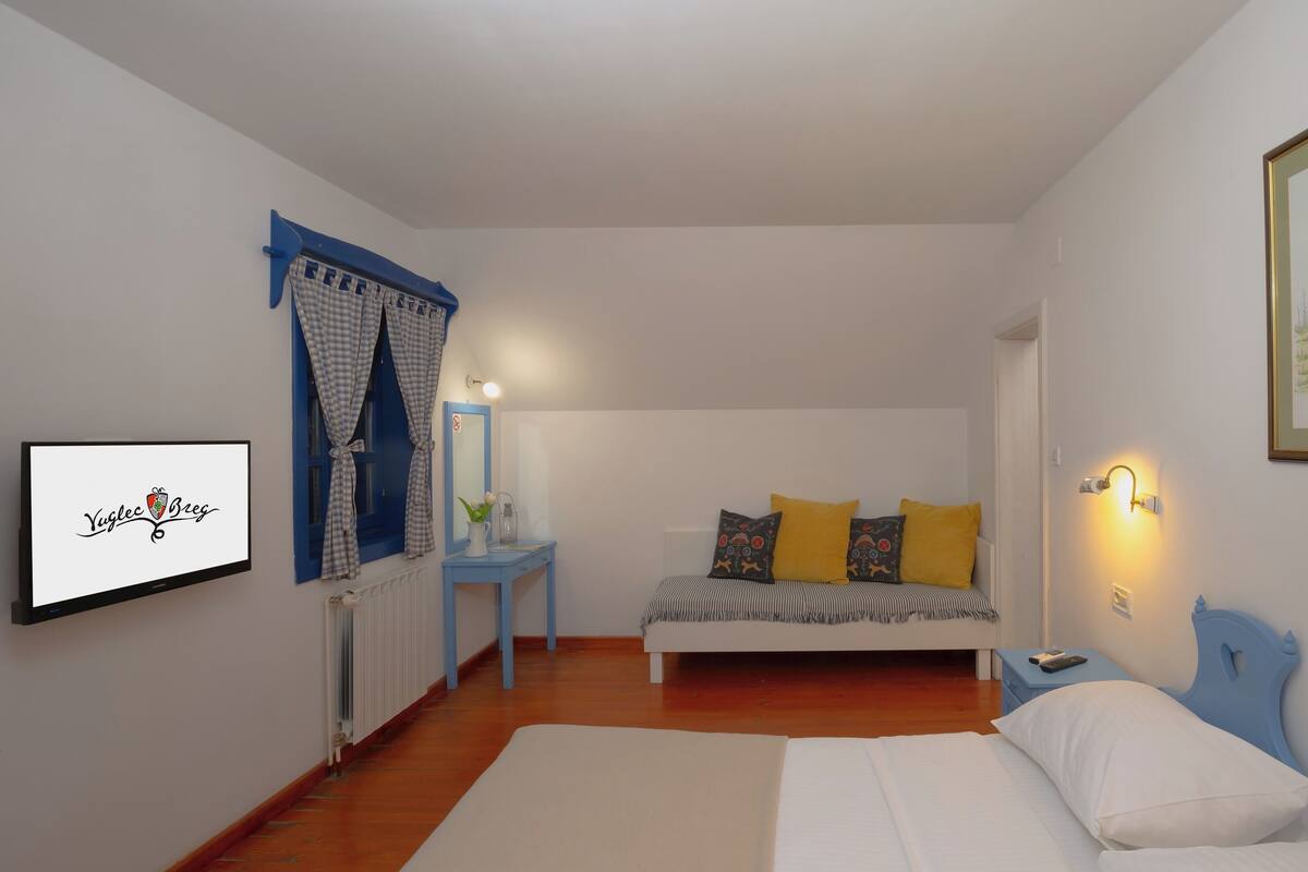 A bedroom with a bed, bedside table, and a wall-mounted TV displaying 'Yuglec Breg'.