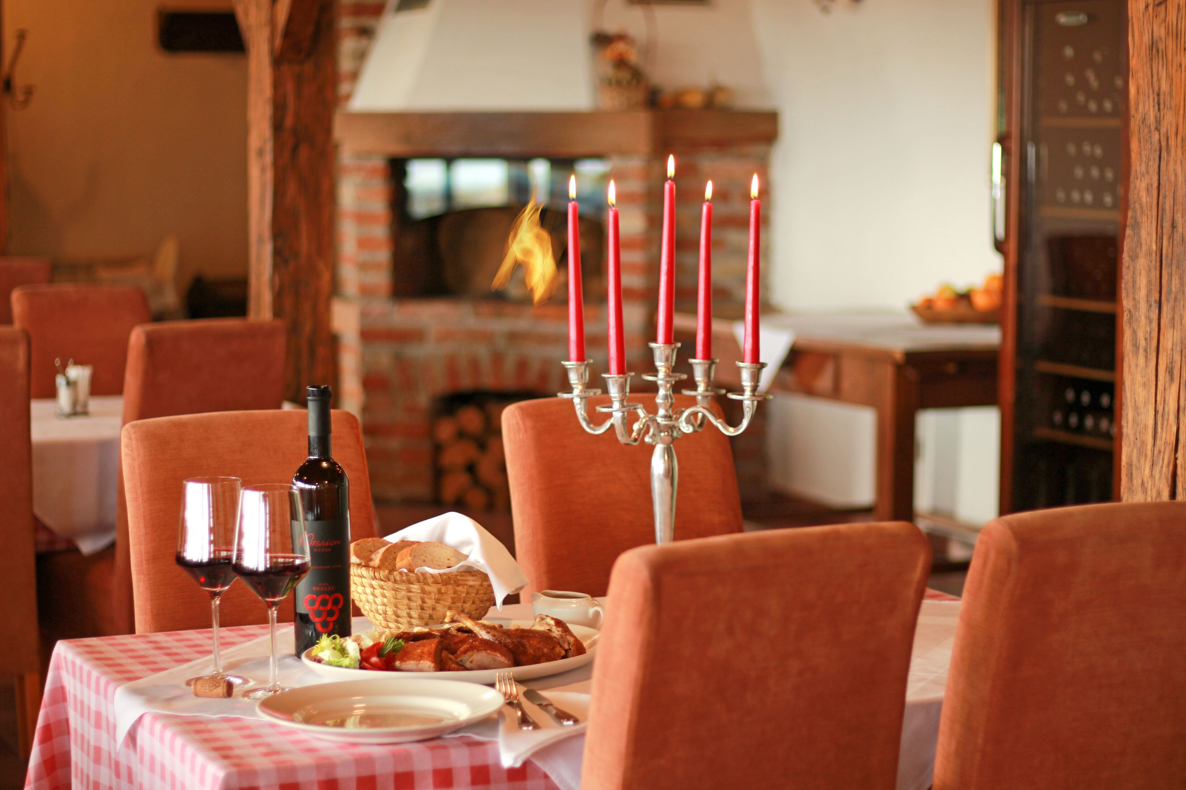 Uma mesa de jantar com toalha xadrez, candelabro com velas acesas, copos de vinho, garrafa de vinho e cesta de pão.
