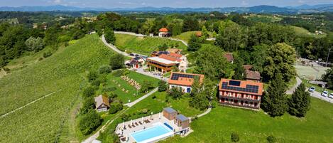 An aerial view of a resort with a swimming pool, multiple buildings, and surrounding greenery.