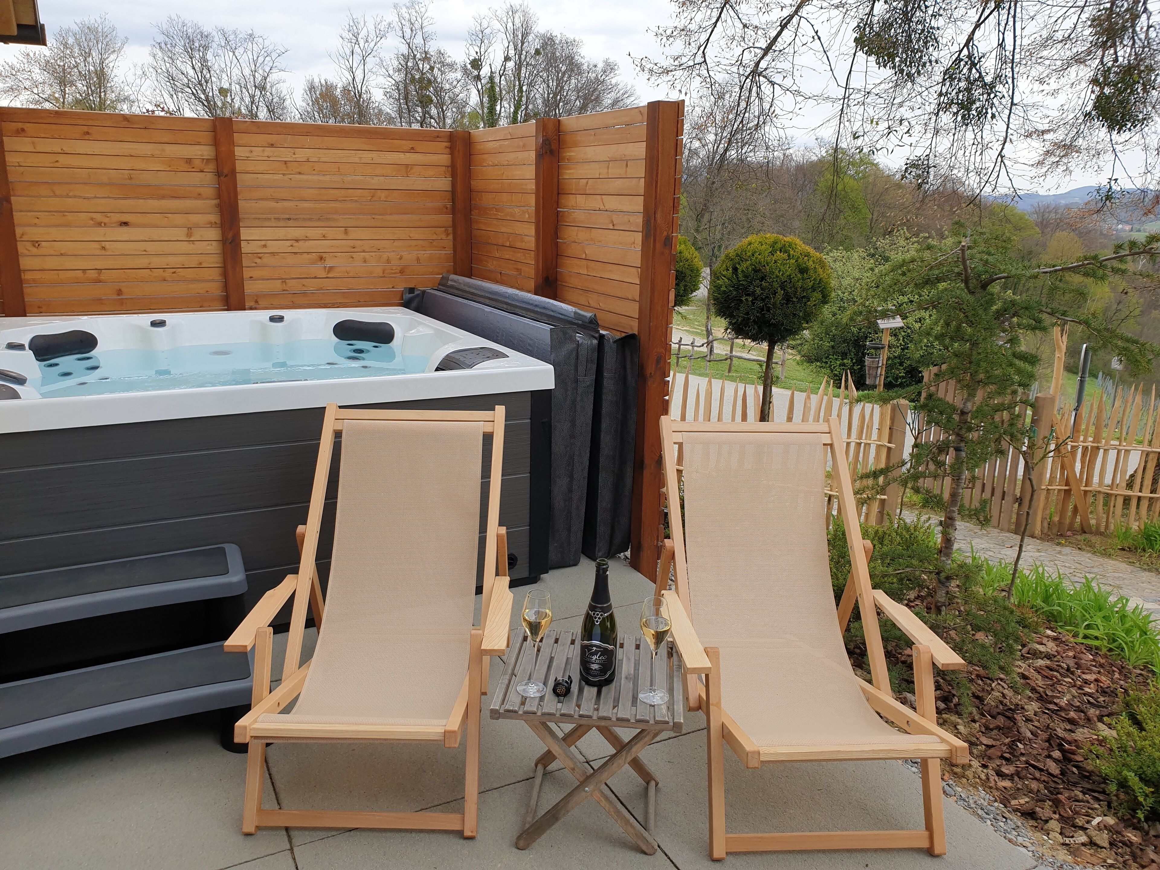 Un jacuzzi con dos sillones de madera y una botella de vino sobre una mesa.