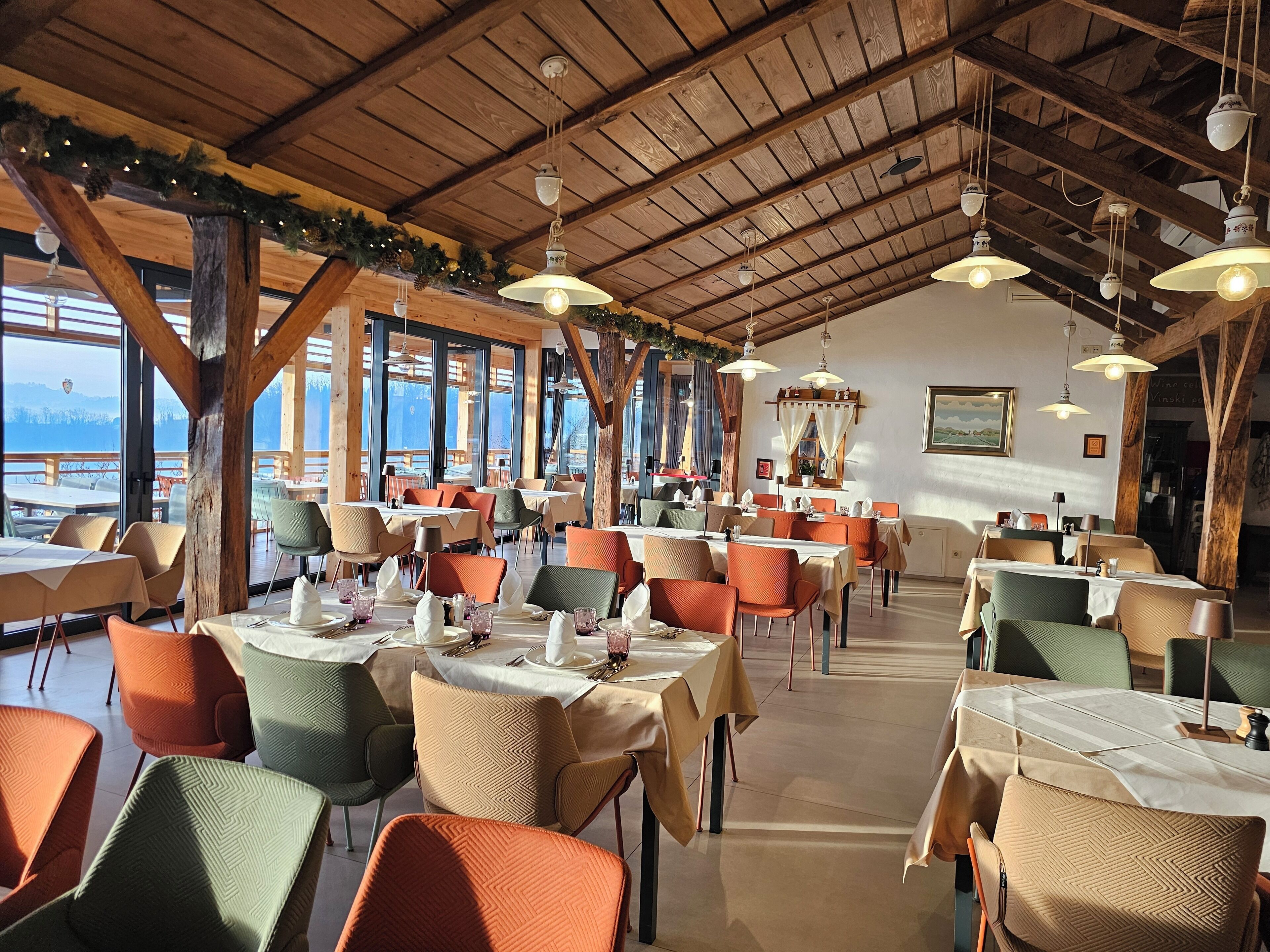 A restaurant with wooden beams, large windows, and tables set for dining.