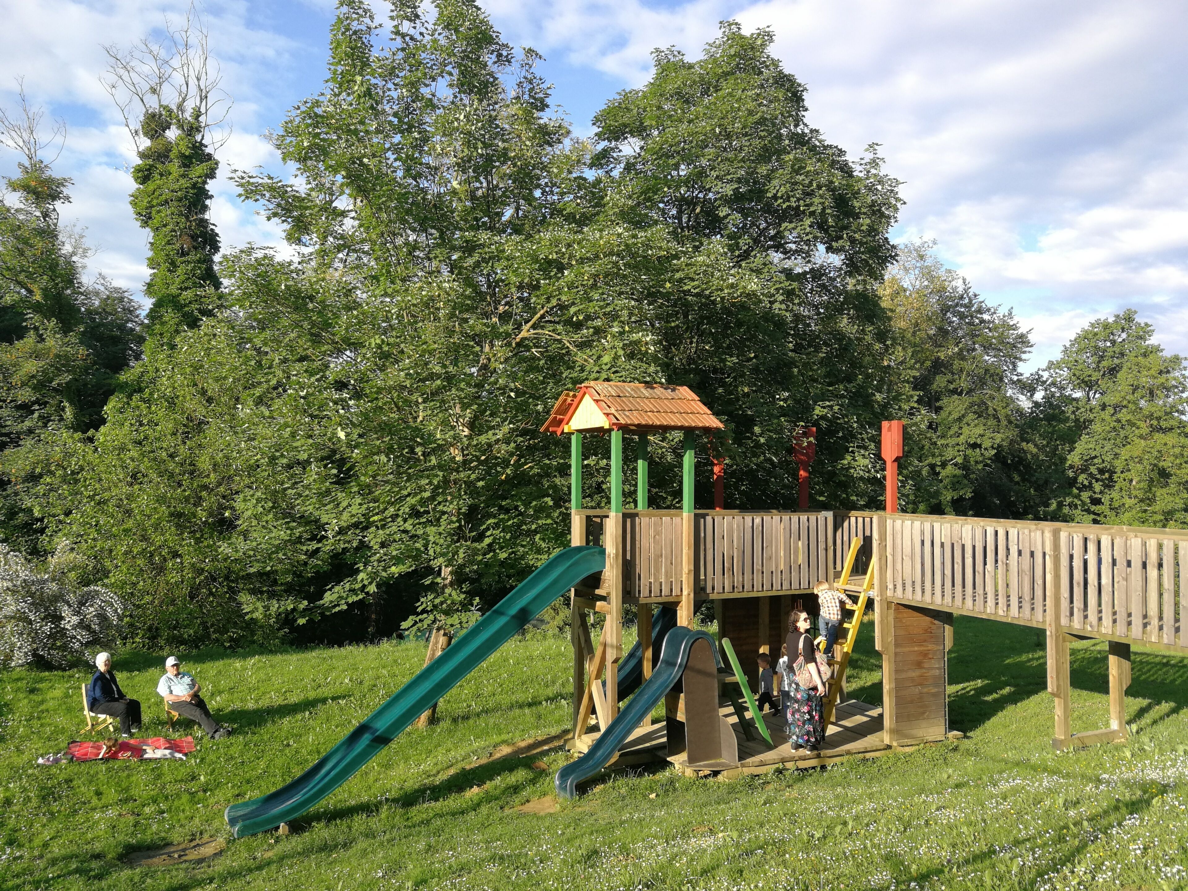 A playground with a slide and climbing structures, surrounded by trees and grass.