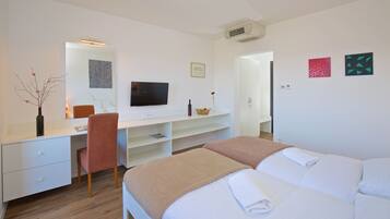 Una habitación de hotel con una cama, un escritorio con computadora, una silla, un televisor y obras de arte en las paredes.