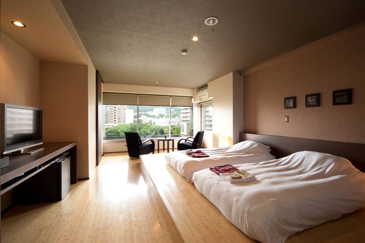 A hotel room with a bed, a TV, a desk, and a view of the city.
