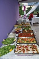 Uma mesa de buffet com diversos pratos e uma parede roxa ao fundo.