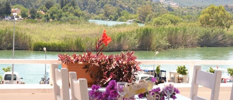 Ein Tisch mit Stühlen am Flussufer, mit Blick auf eine üppige grüne Landschaft mit Hügeln in der Ferne.