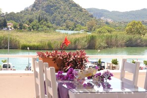 A table with chairs set up by a riverside, overlooking a lush green landscape with hills in the distance.