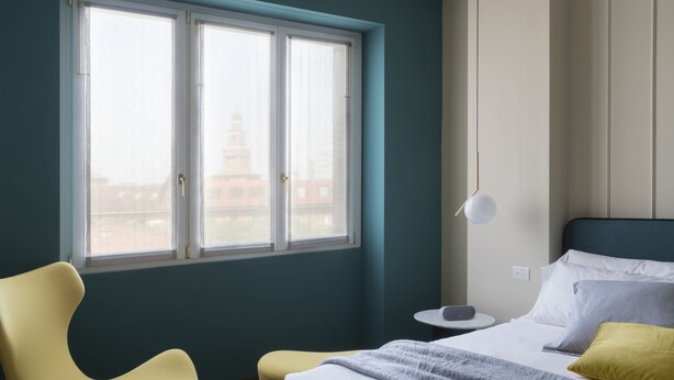 A hotel room with a bed, a chair, a bedside table, and a window with a view of buildings. - Castello Sforzesco Suites by Brera Apartments (Milan)