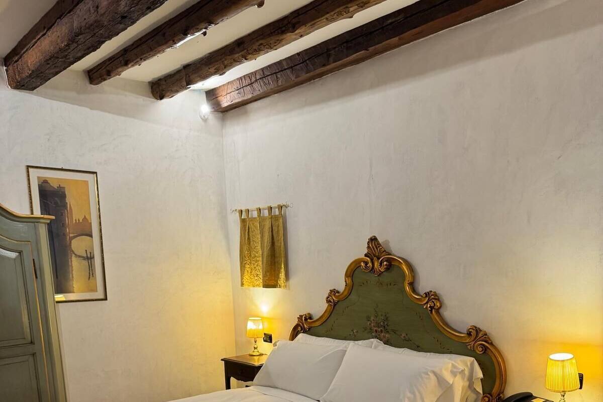 A bedroom with a bed, two bedside tables with lamps, a wooden headboard, a framed picture on the wall, and a door.