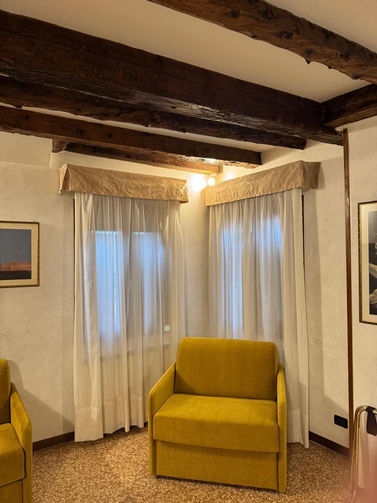 A room with a yellow armchair, a wooden ceiling, and white curtains.