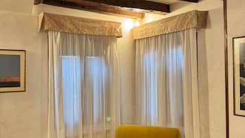 A room with a yellow armchair, a wooden ceiling, and white curtains.