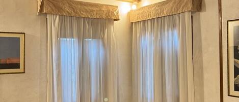 Una habitación con un sillón amarillo, techo de madera y cortinas blancas.