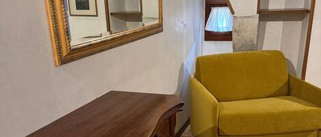 Um quarto com cômoda de madeira, sofá amarelo mostarda, um espelho grande e uma escada.