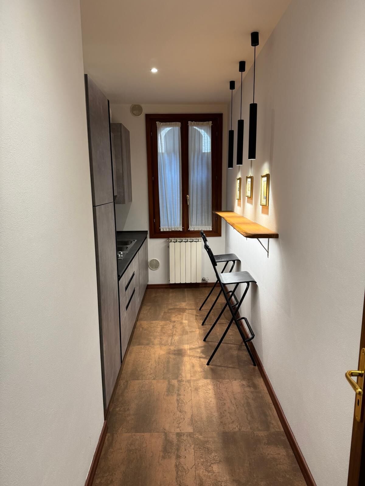 A narrow kitchen with a dining area, a radiator, and a window with curtains.
