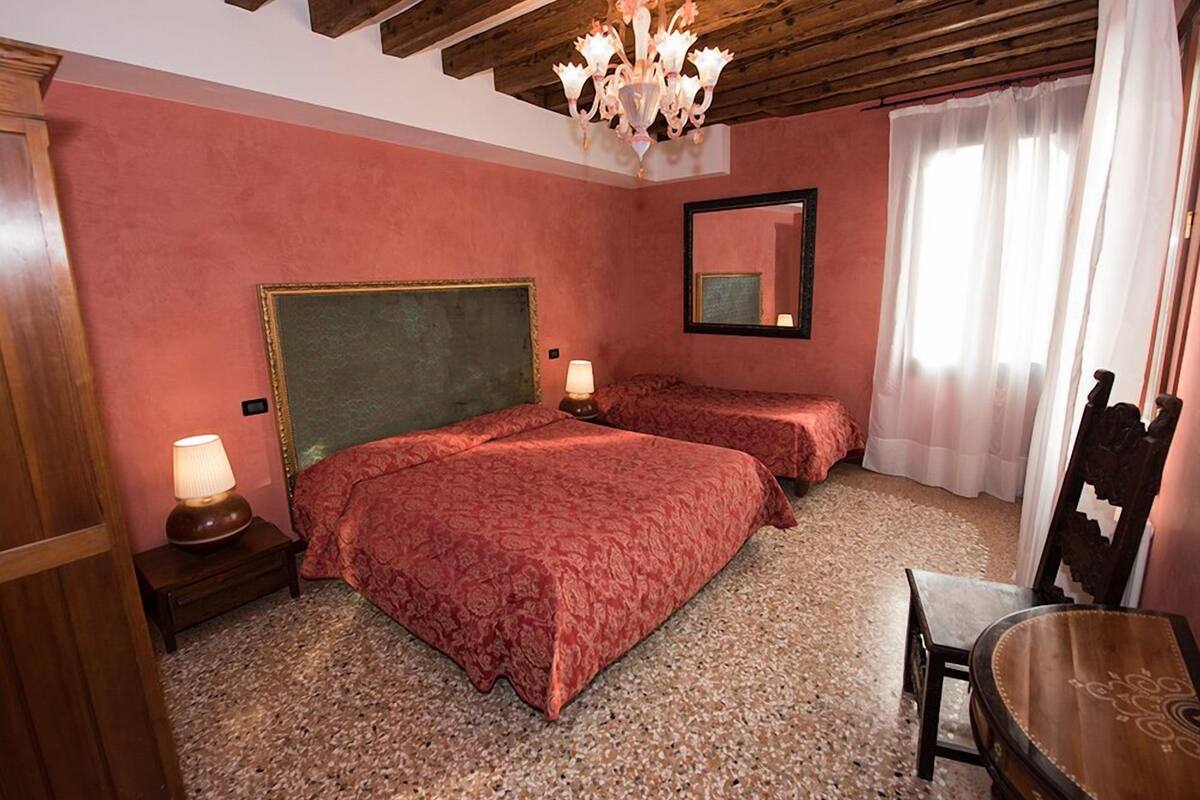 A room with two beds, a wooden ceiling, a chandelier, a mirror, and a small table.
