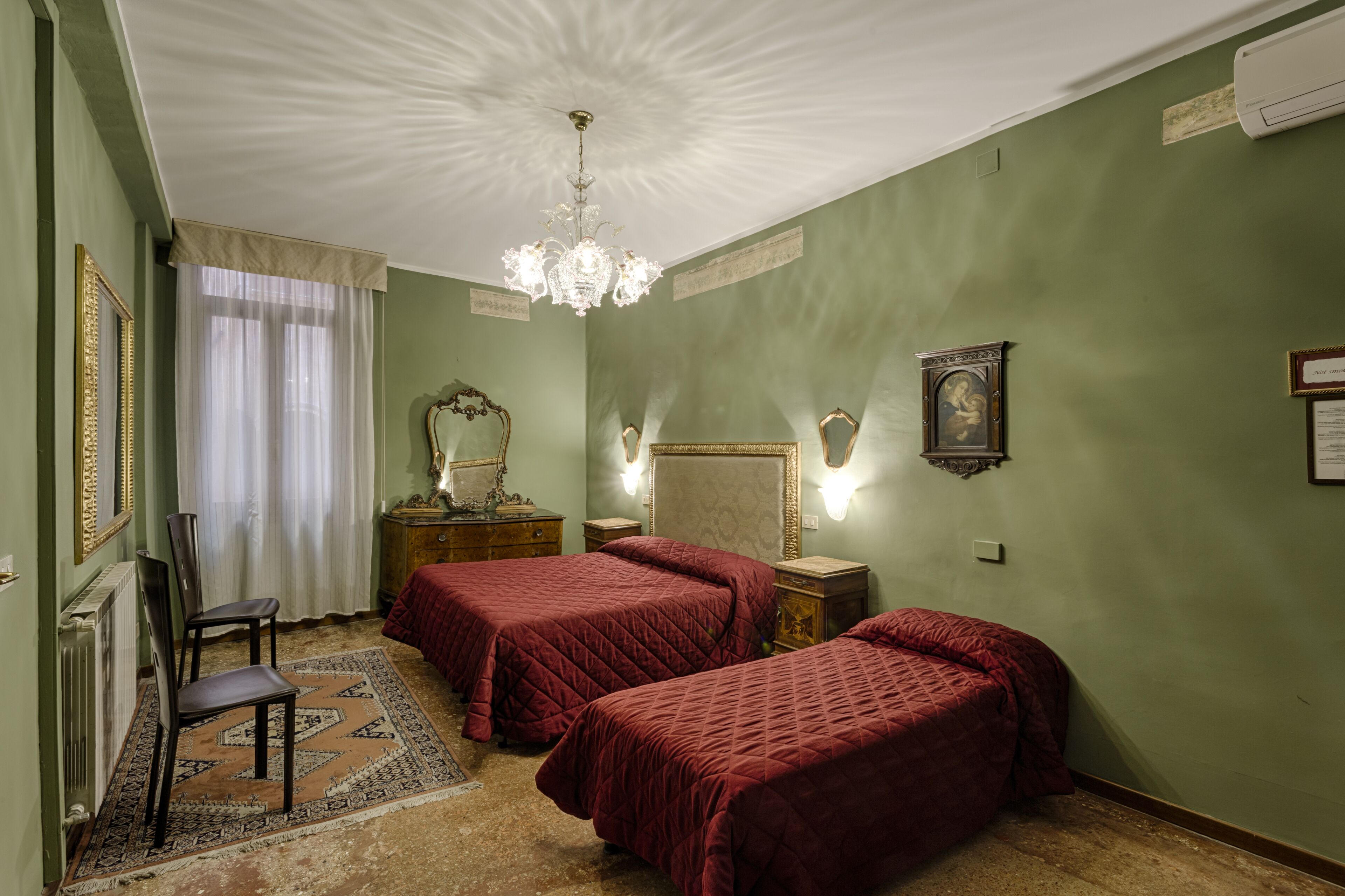A room with two beds, a chandelier, a mirror, and a radiator.
