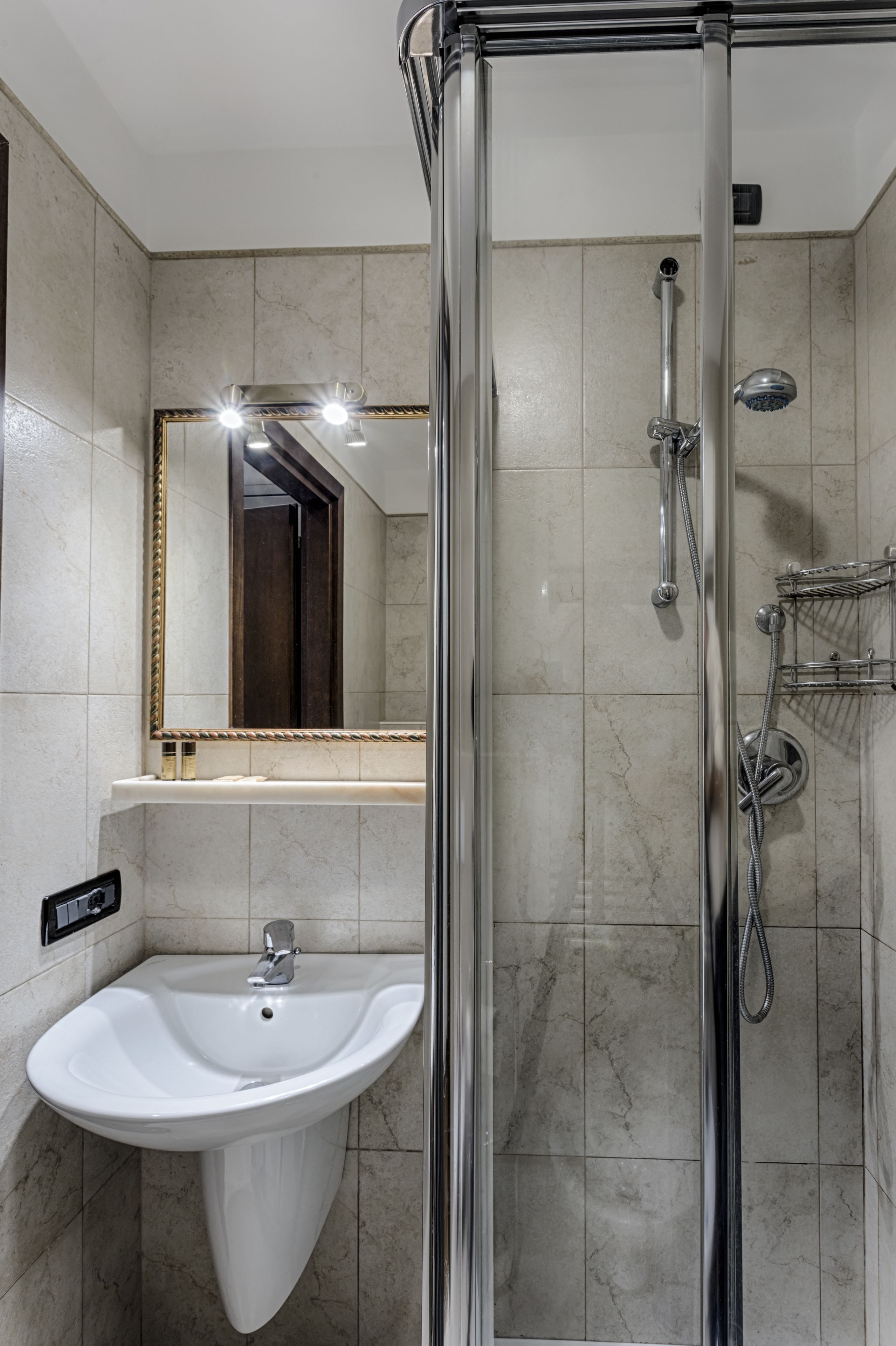 A bathroom with a glass-enclosed shower, a white sink, and a large mirror with lights.