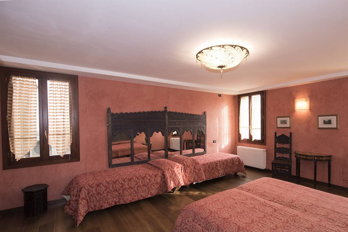 A bedroom with two beds, a wooden headboard, a radiator, and a small table.