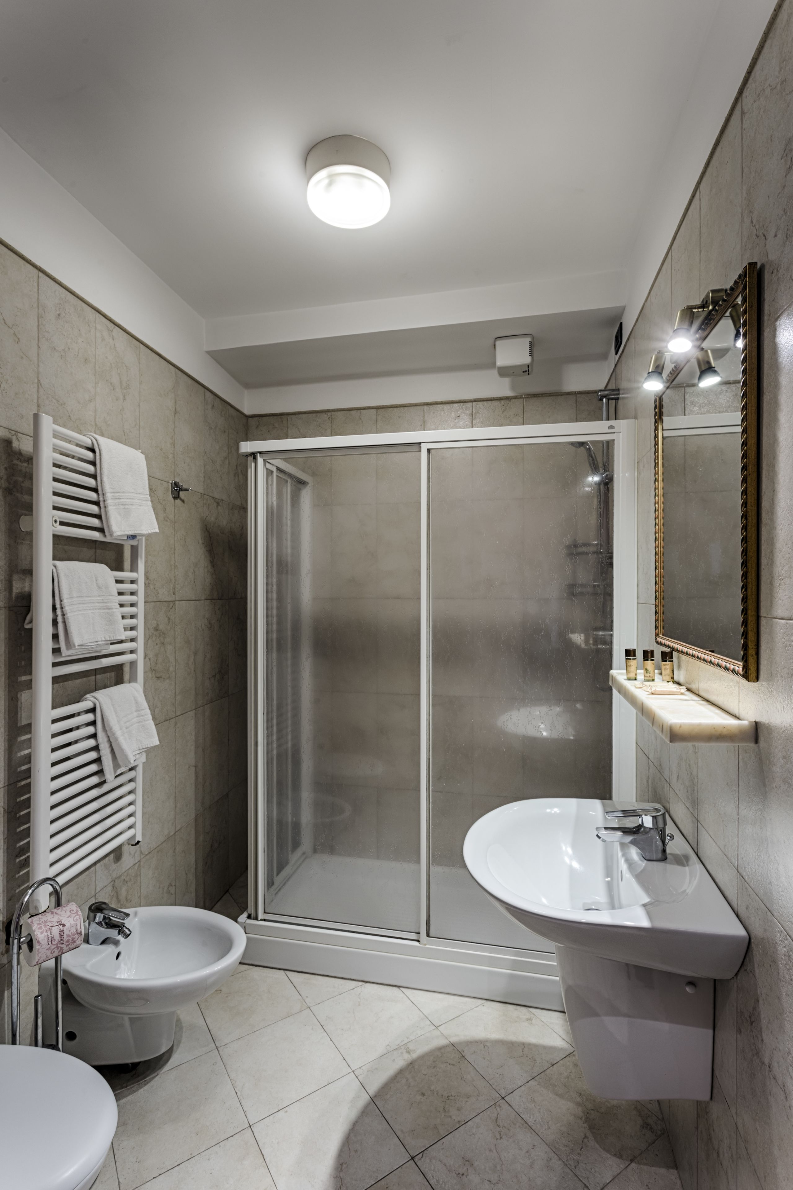 A modern bathroom with a glass shower enclosure, a pedestal sink, and a vanity mirror.
