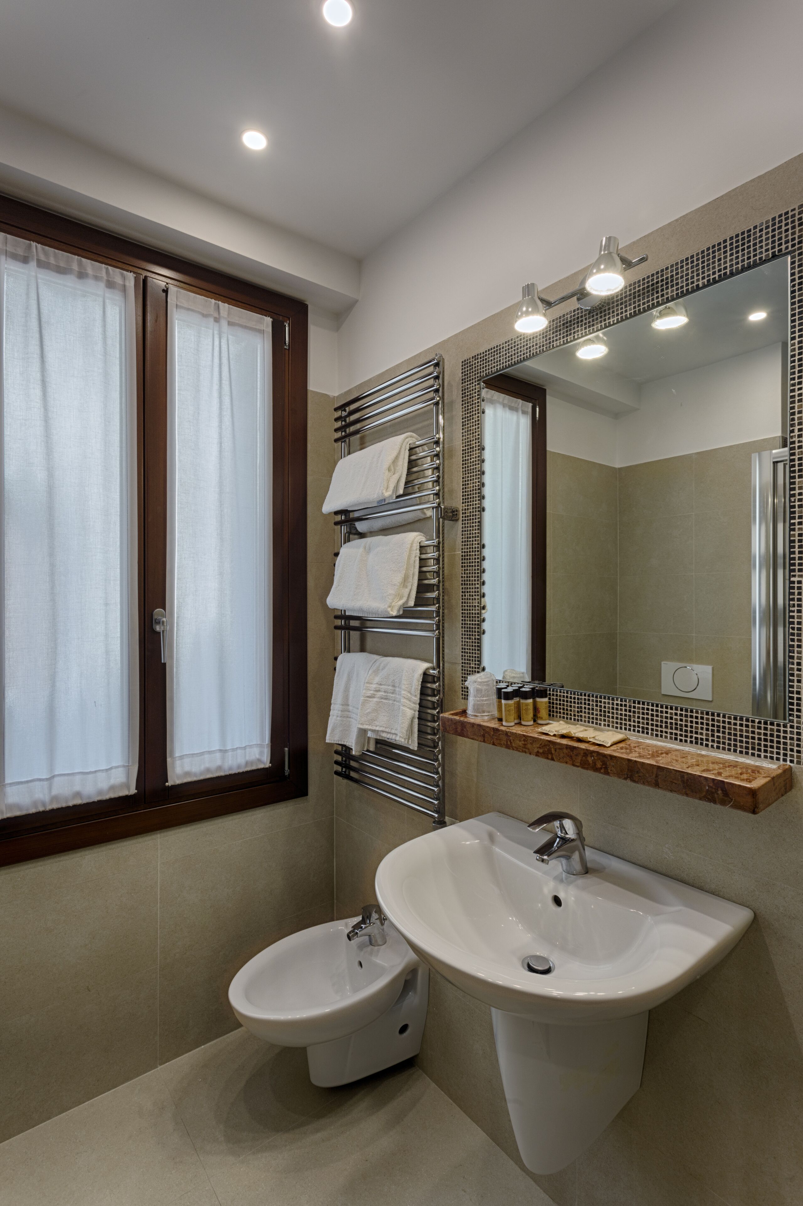 A modern bathroom with two sinks, a bidet, a towel rack, and a large mirror.