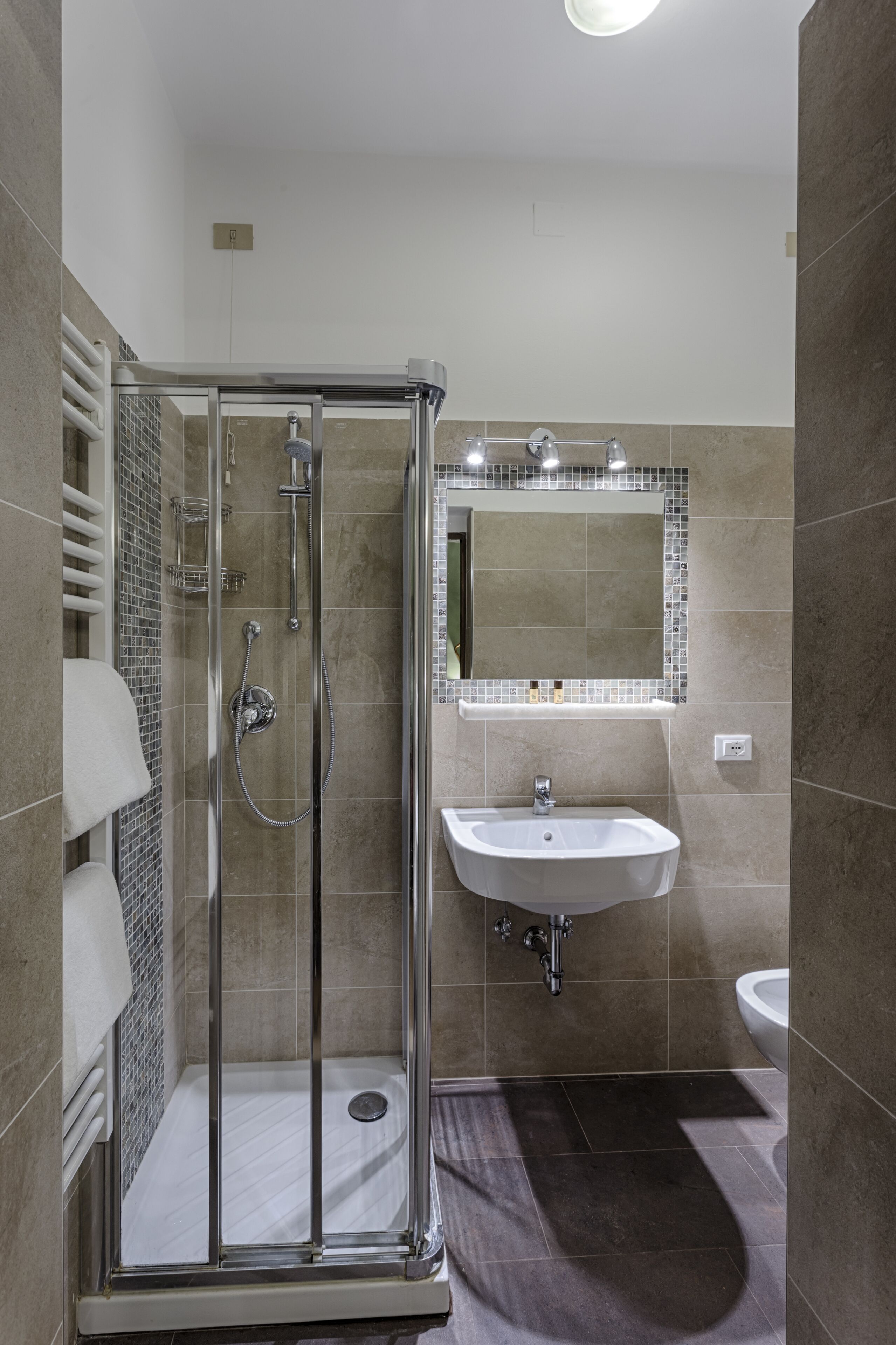 A modern bathroom with a glass-enclosed shower, a white sink, and a large mirror.
