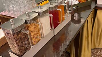 Ein Buffet mit verschiedenen Speisen und Getränken, darunter Müsli, Säfte und Kaffee.