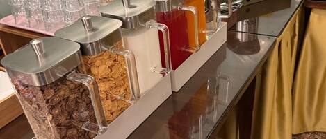A buffet setup with various food and drink dispensers, including cereal, juices, and coffee.