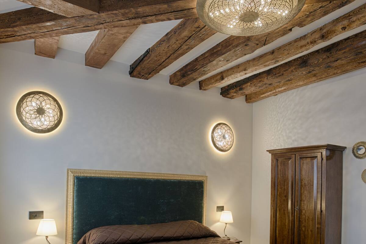 A bedroom with a large bed, wooden beams, a round ceiling light, and a wooden wardrobe.