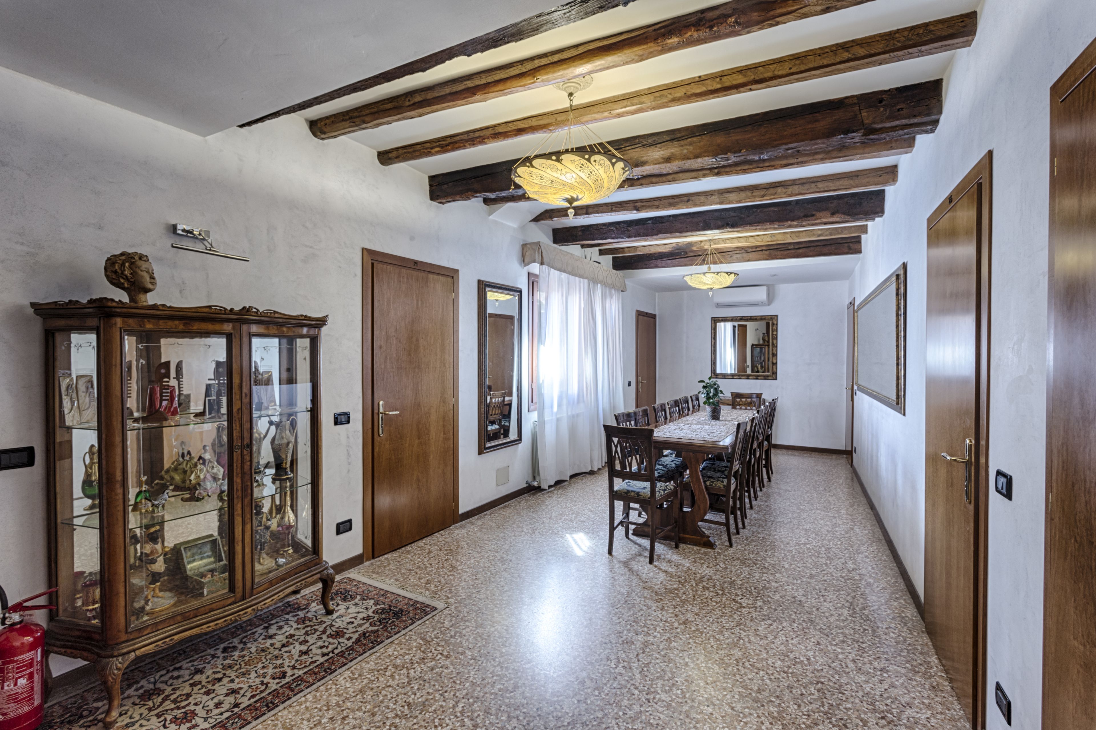 A dining area with a wooden table and chairs, a cabinet with glass doors, and a chandelier.