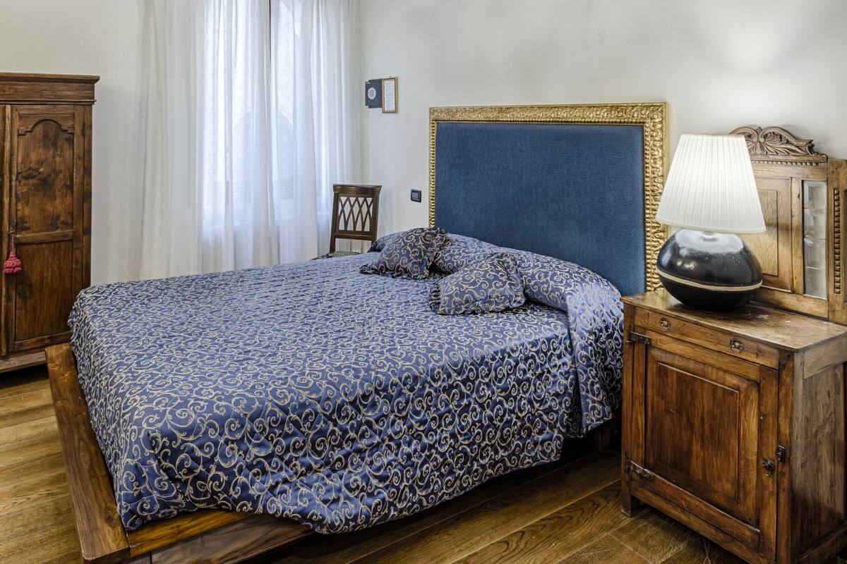 A bedroom with a wooden ceiling, a bed with a blue headboard, a wooden nightstand, and a chandelier.