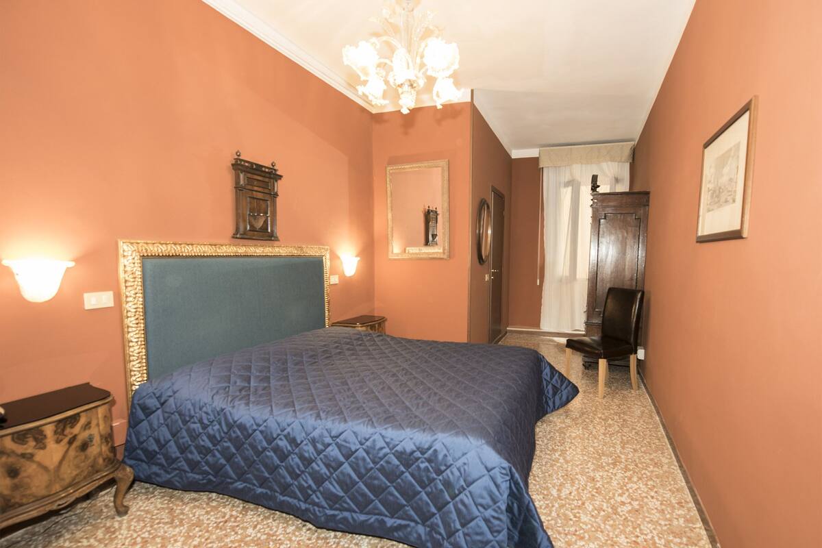 A bedroom with a large bed, a dresser, a mirror, and a door leading to another room.
