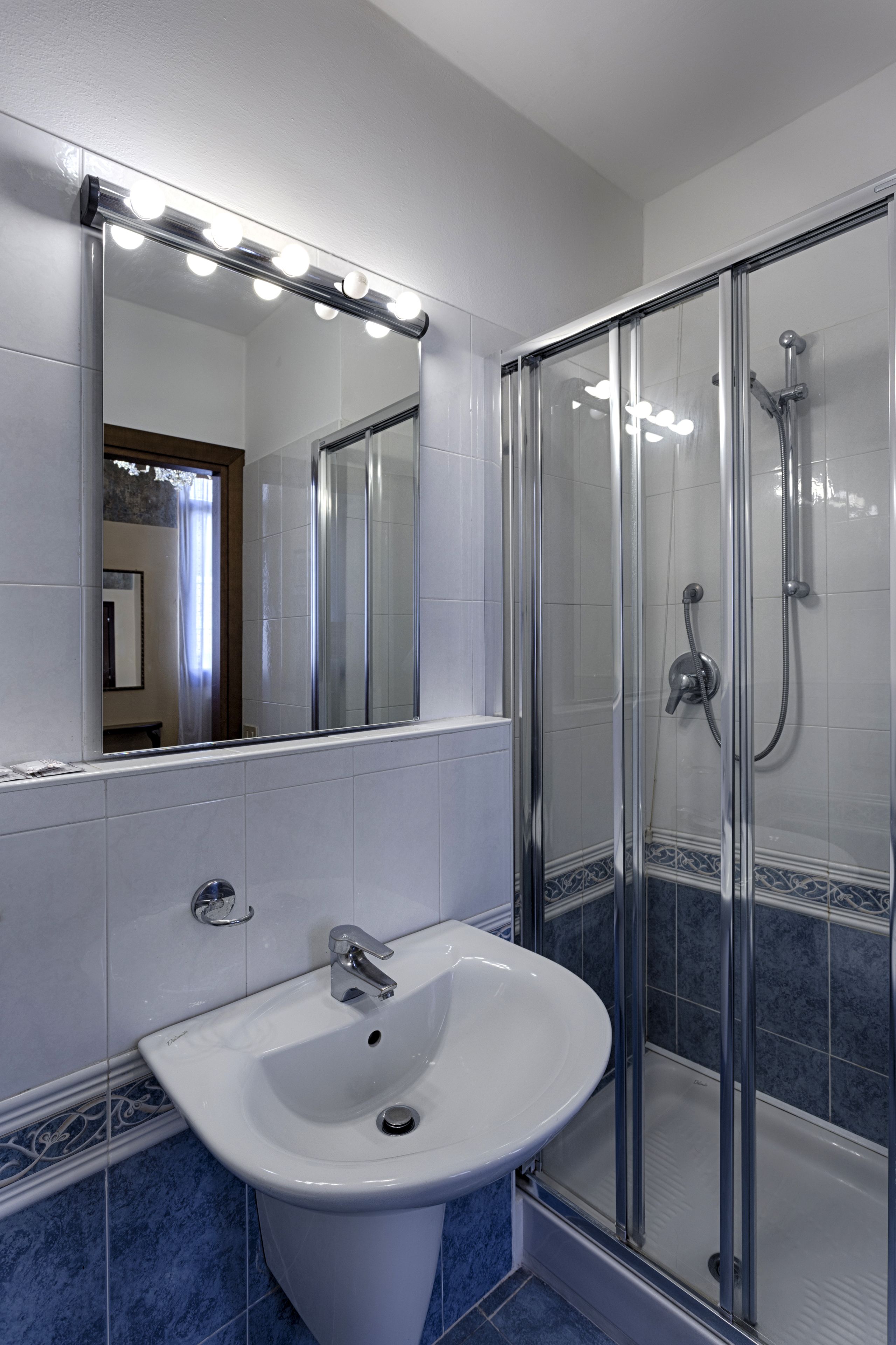 A bathroom with a white sink, a large mirror with lights, and a glass shower enclosure.