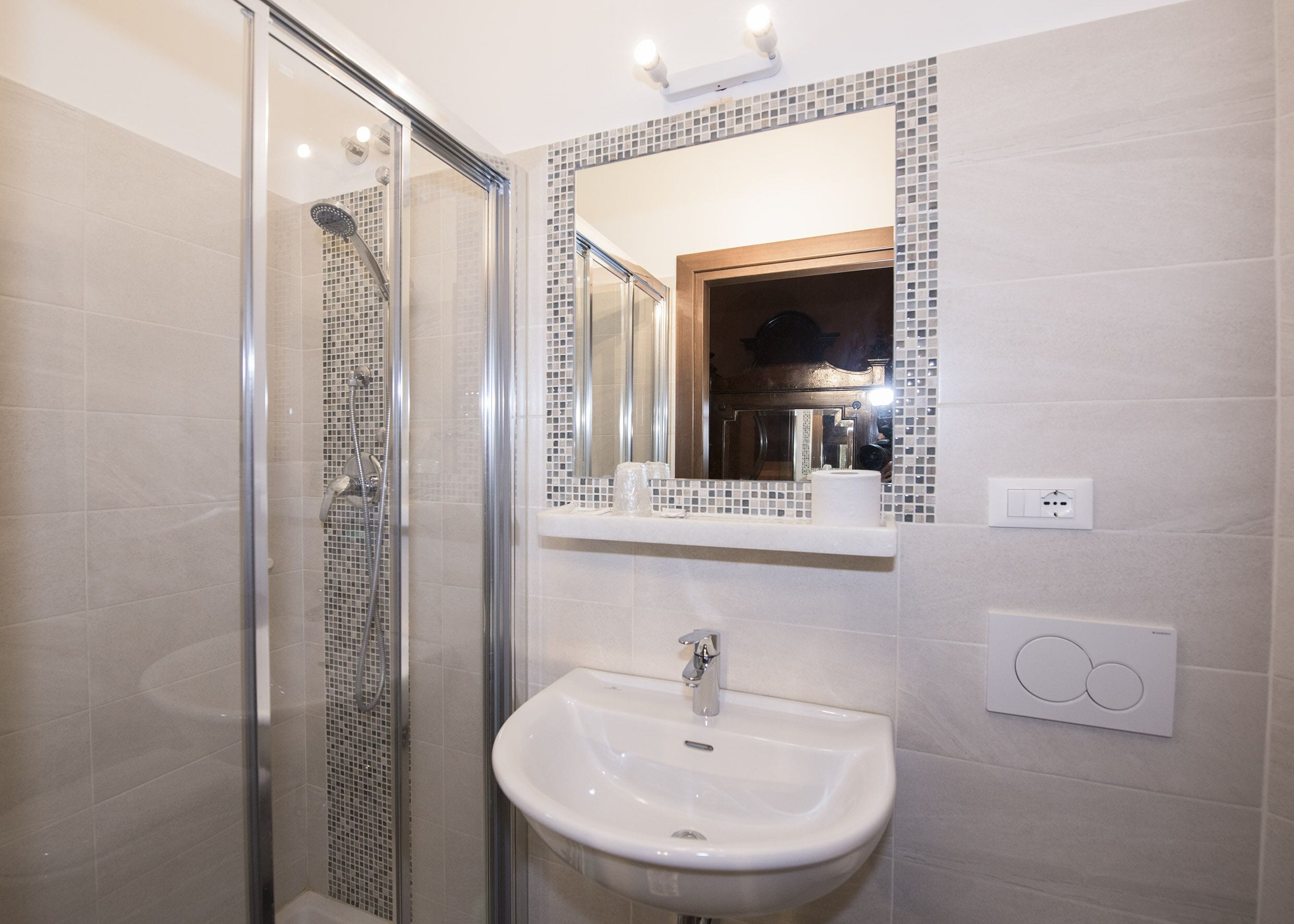 Un baño moderno con ducha de vidrio, lavamanos blanco y salpicadero de azulejos.