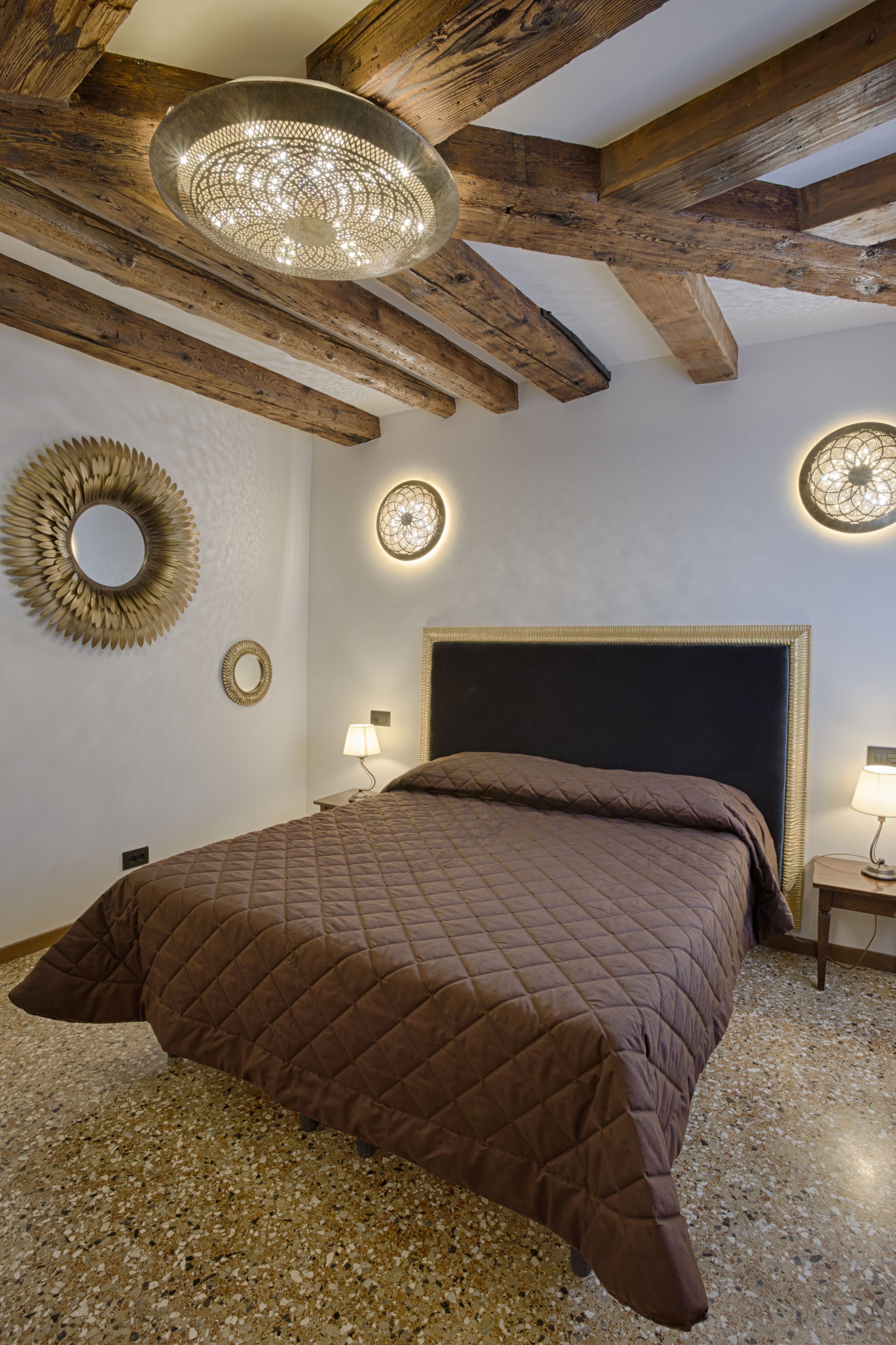 A bedroom with a large bed, wooden beams, and decorative wall sconces.
