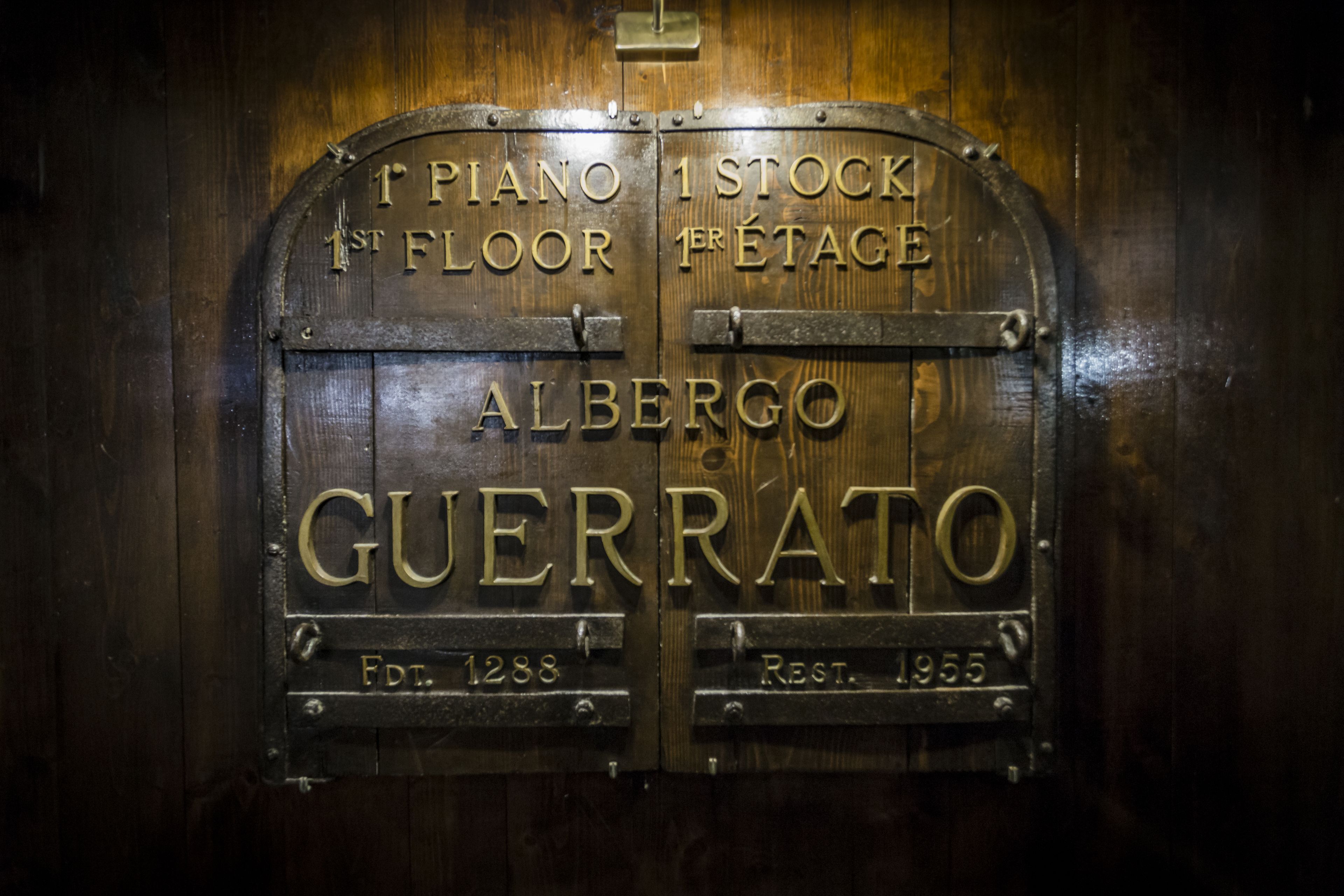 Une porte en bois portant le nom « Alberto Guerrato » et les inscriptions « Piano 1er étage » et « Stock 1er étage ».