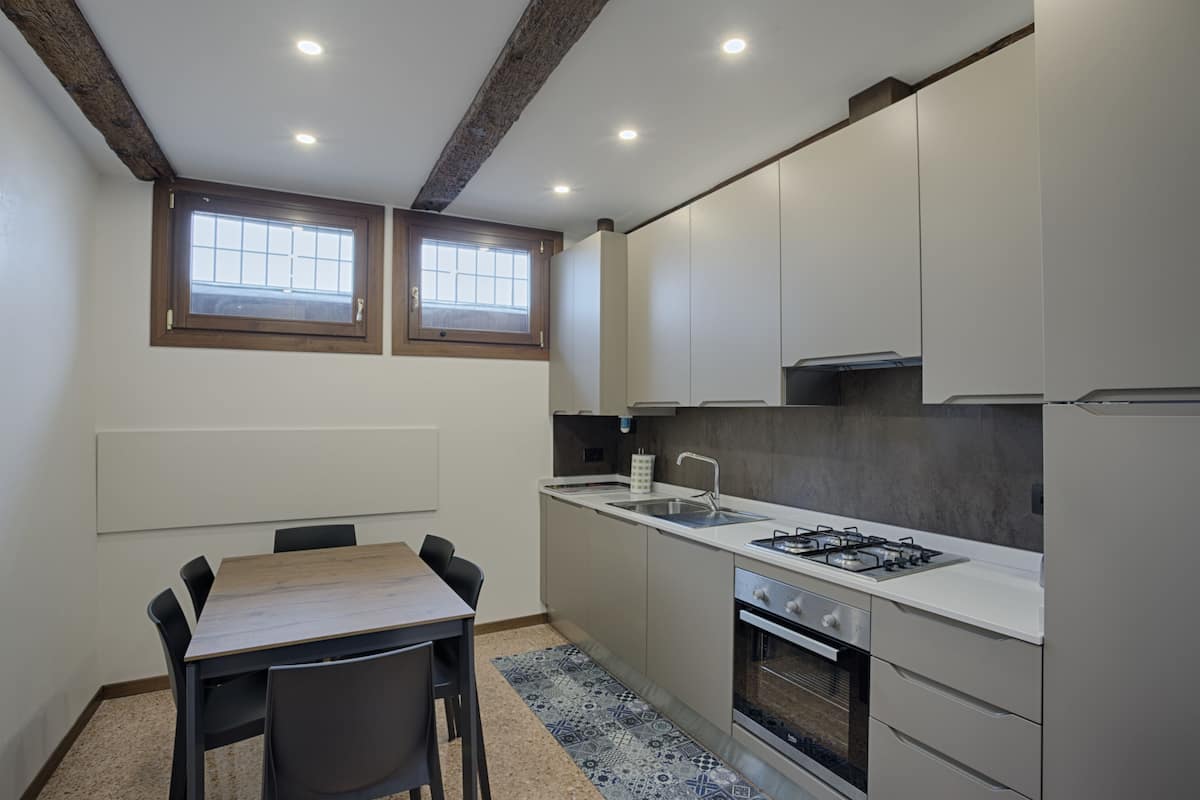 A compact kitchen with a dining table, two windows, and a built-in oven.