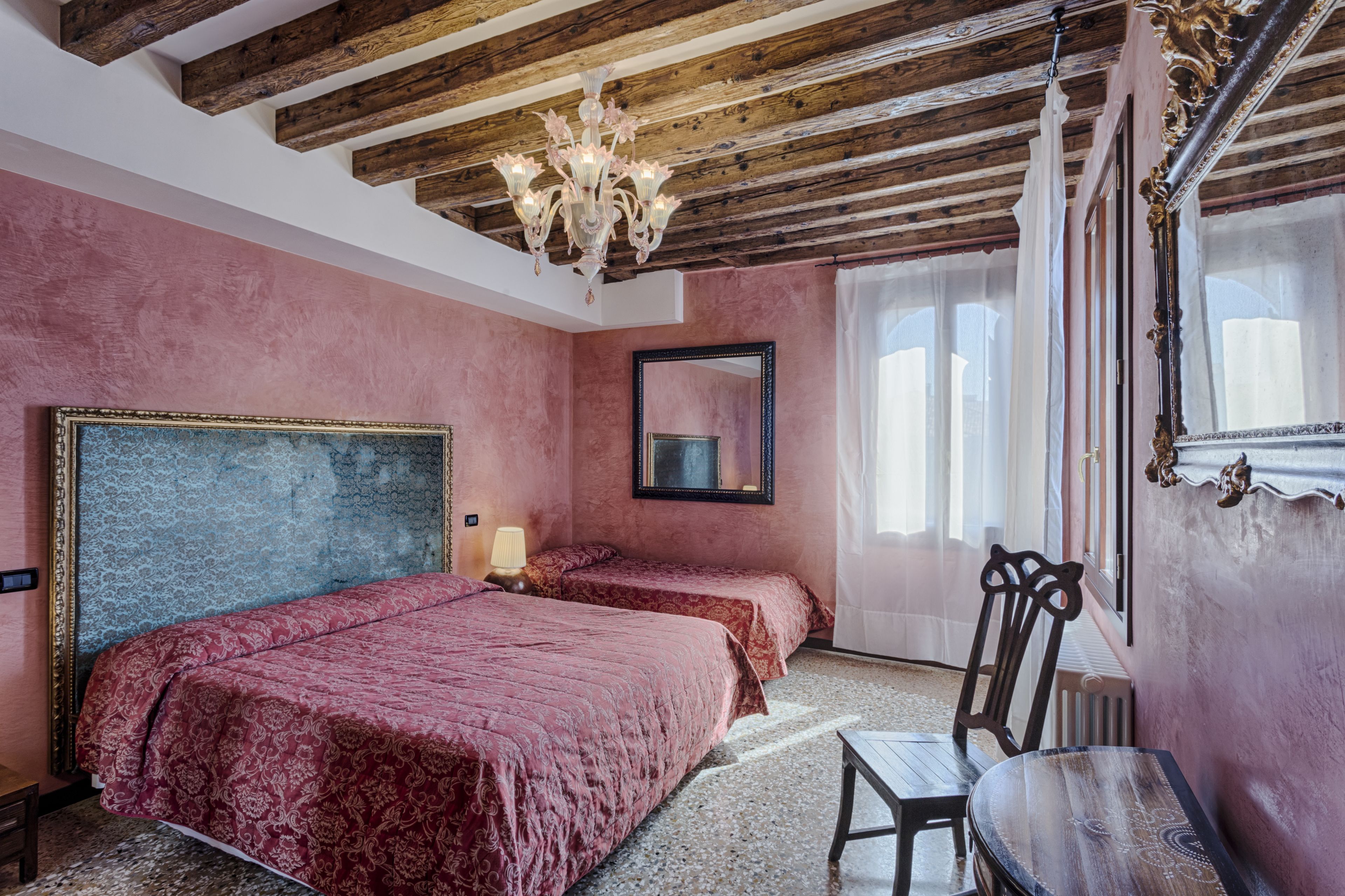 A bedroom with two beds, a chandelier, a mirror, and a window with curtains.