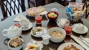 Un comedor con varias mesas dispuestas para el desayuno, incluyendo platos, tazones y una cesta de pan.