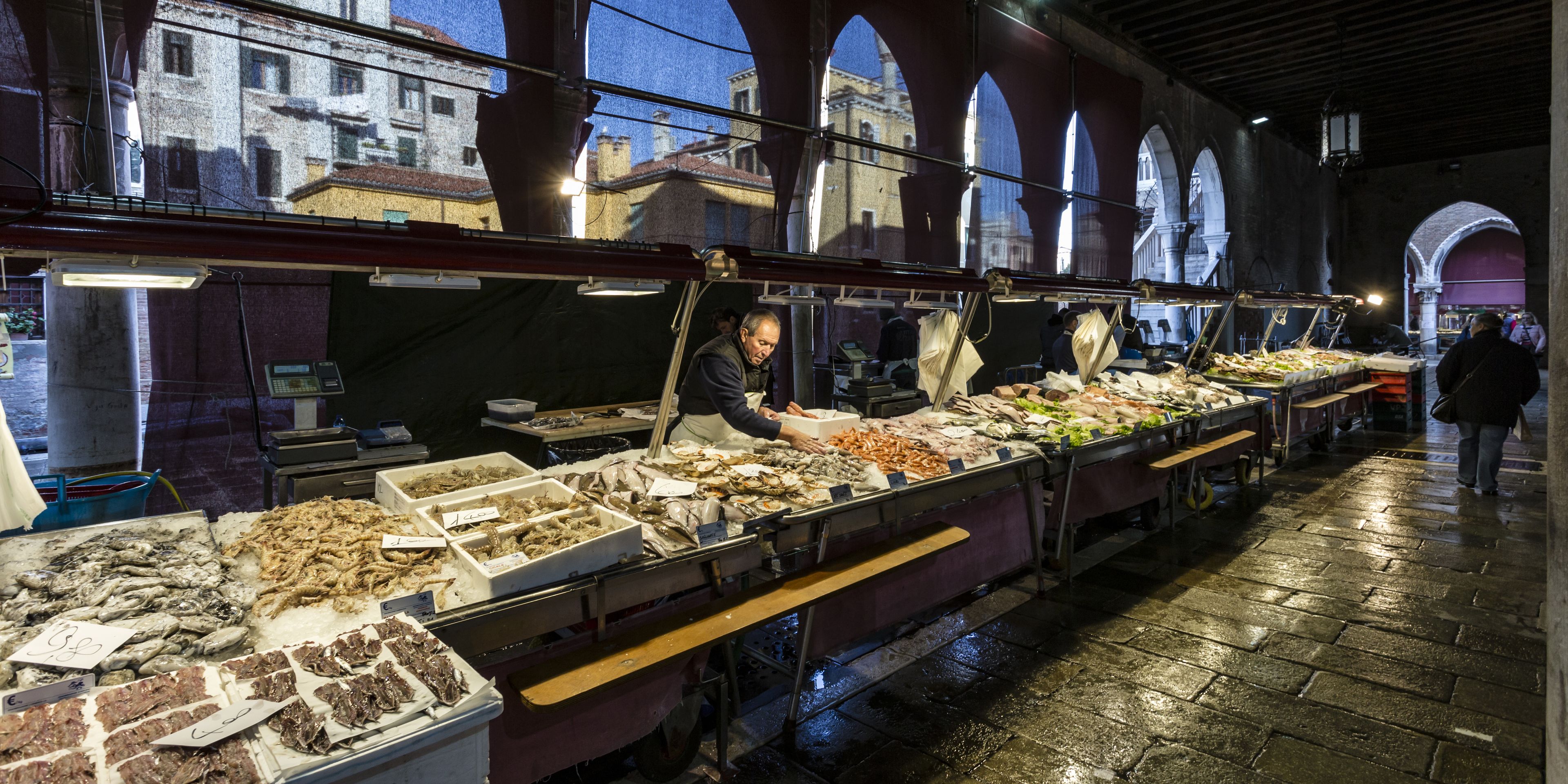 Un mercado de mariscos con varios pescados exhibidos sobre hielo, bajo una zona techada con arcos.