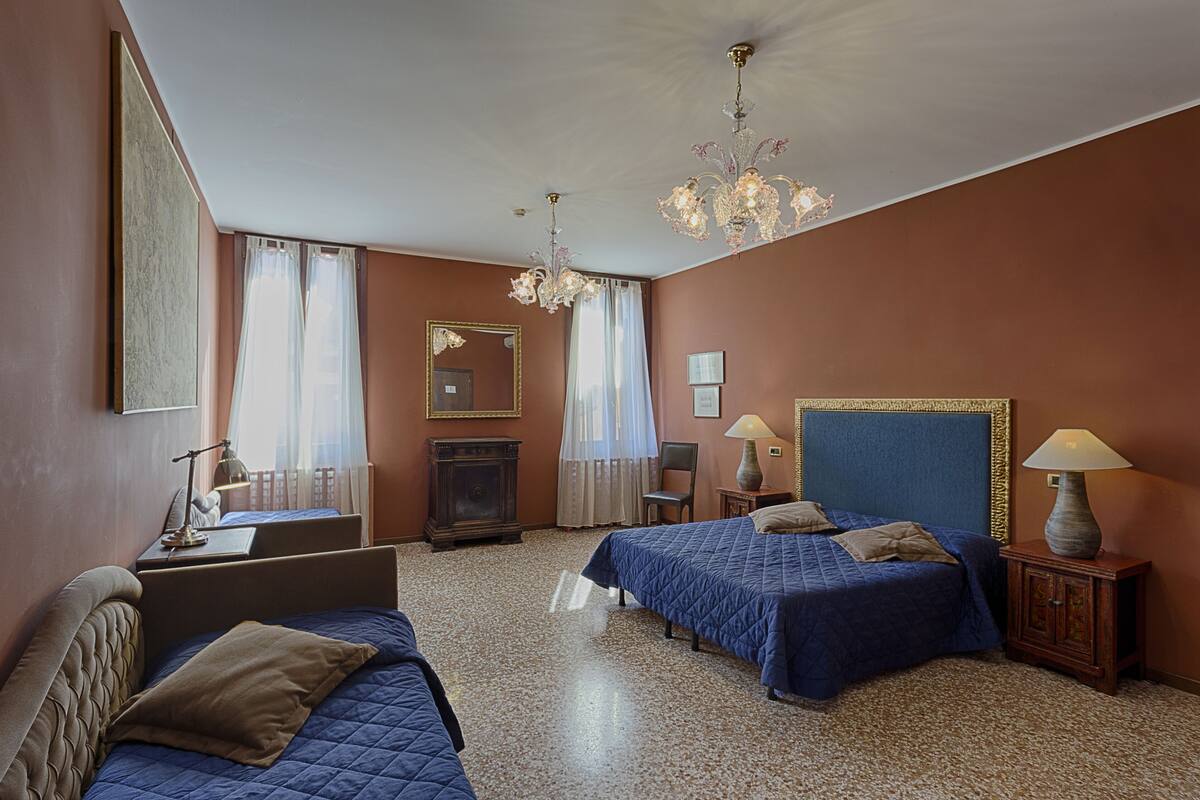 A hotel room with two beds, a desk, a chair, a lamp, and a chandelier.
