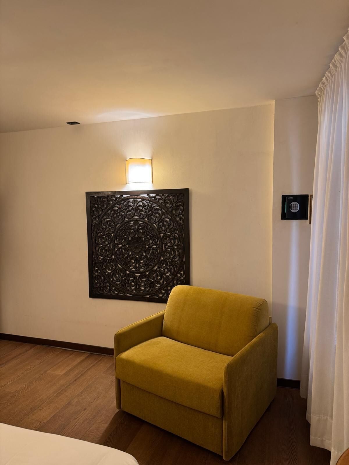 Habitació d'hotel amb una butaca groga, un panell decoratiu a la paret, una lluminària i una porta amb pestanya.
