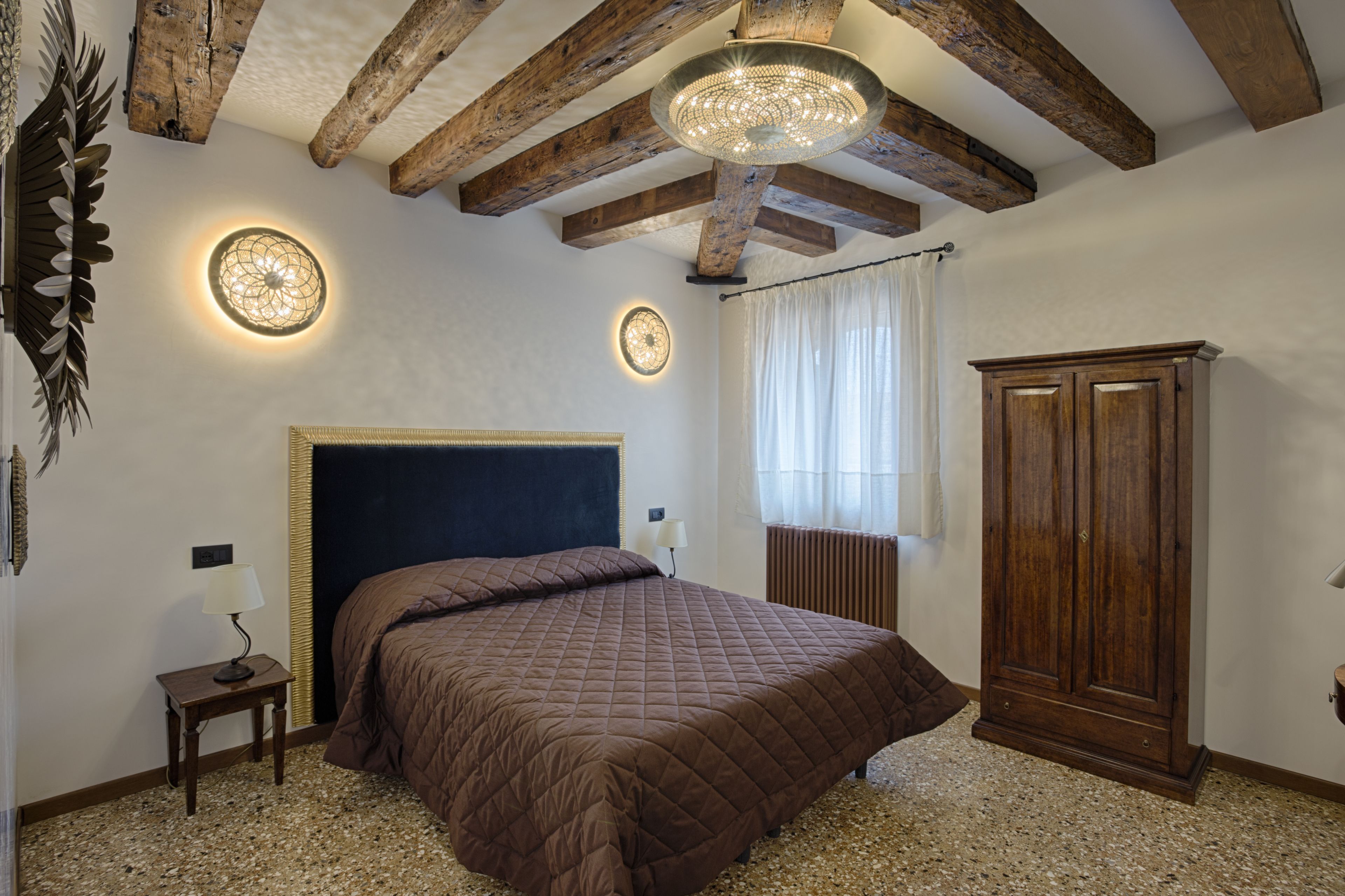 A bedroom with a large bed, wooden beams, a ceiling light fixture, and a wardrobe.