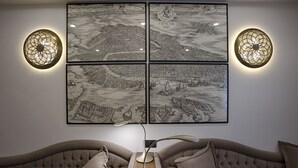 Una habitación con un sofá capitonado, una lámpara de pie moderna y cuatro mapas en blanco y negro enmarcados en la pared.