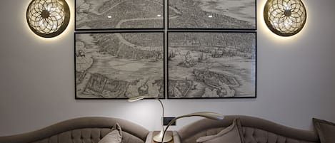 A room with a tufted sofa, a modern floor lamp, and four framed black and white maps on the wall.
