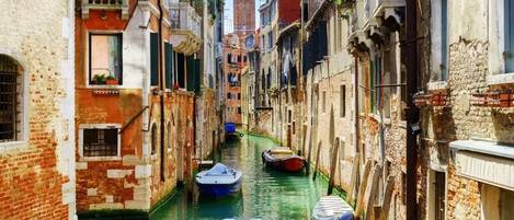 Un canal estrecho en una ciudad histórica, con edificios a ambos lados y una torre al fondo.