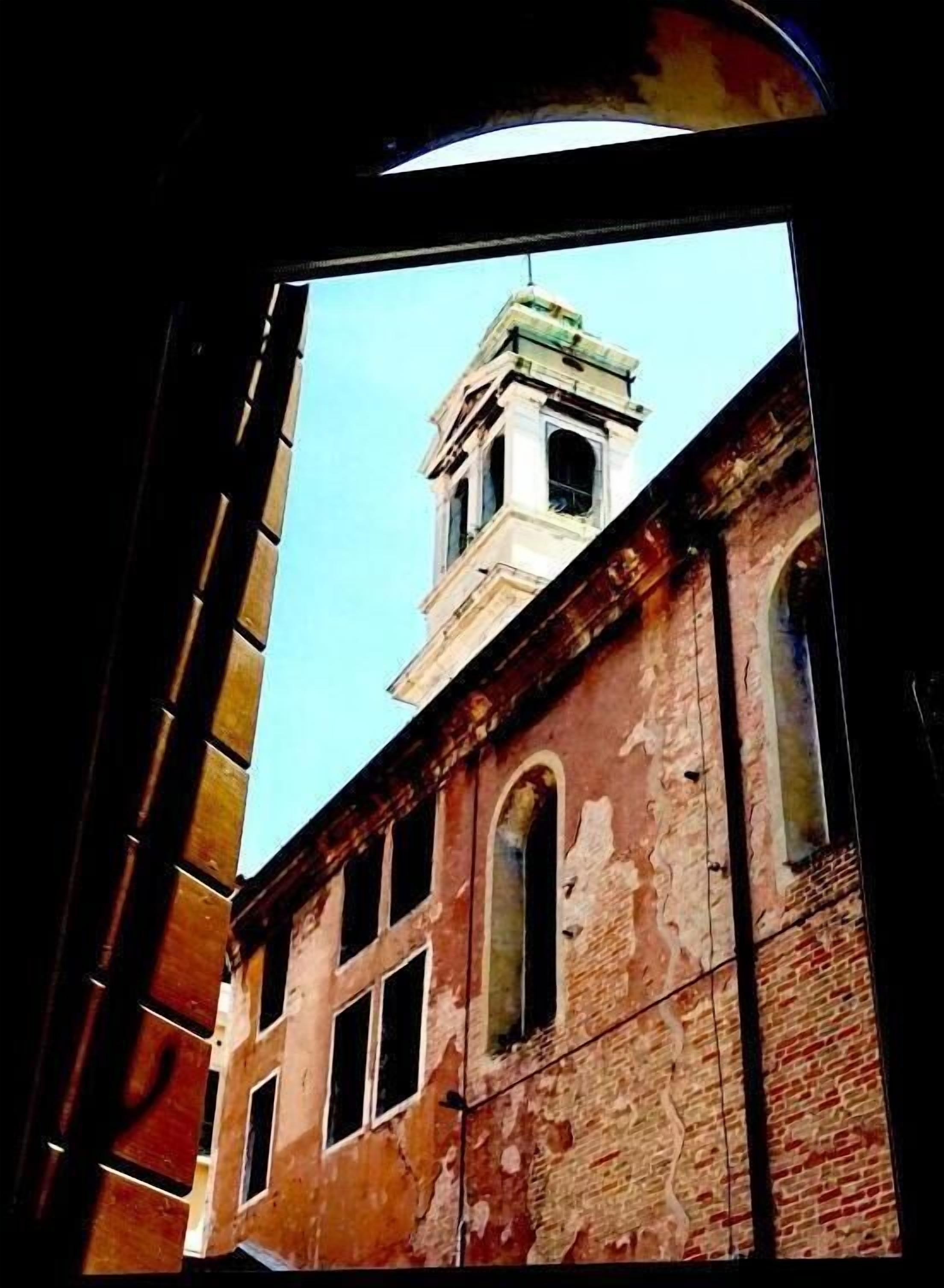 Vista de un edificio histórico con una torre de reloj, a través de una ventana con marco de madera.