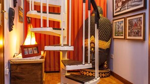 A spiral staircase with a white railing, a decorative lamp, and a large golden statue in a room with wooden flooring and striped wallpaper. - Casa Kita (Cortona)