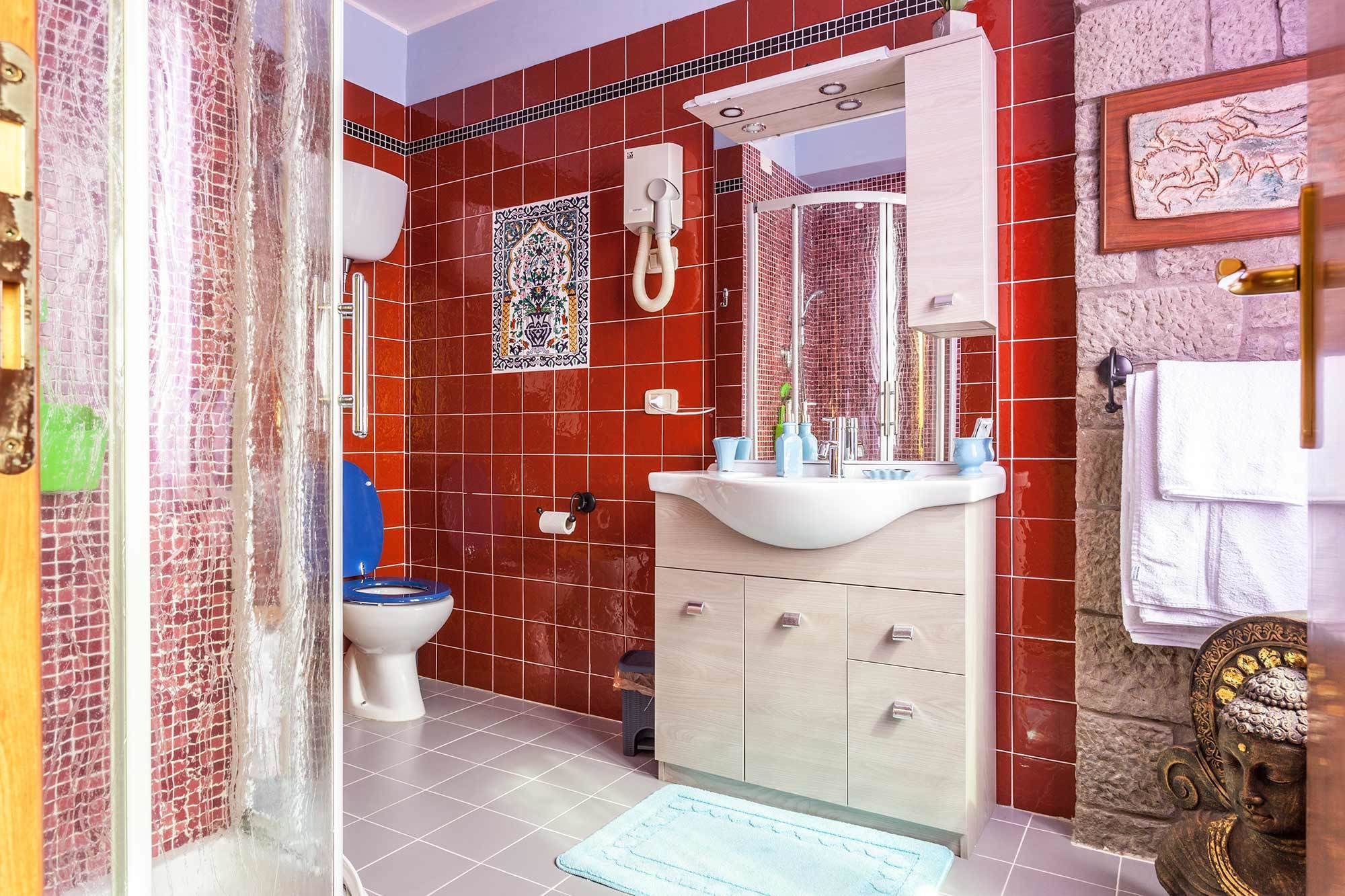 Ein Badezimmer mit roten Fliesenwänden, einem weißen Waschbecken, einer blauen Toilette und einer Duschkabine.