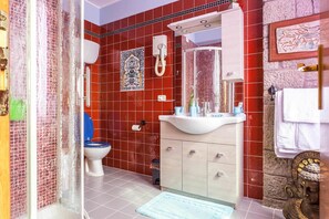 Un baño con paredes de azulejos rojos, un lavamanos blanco, un inodoro azul y una zona de ducha.