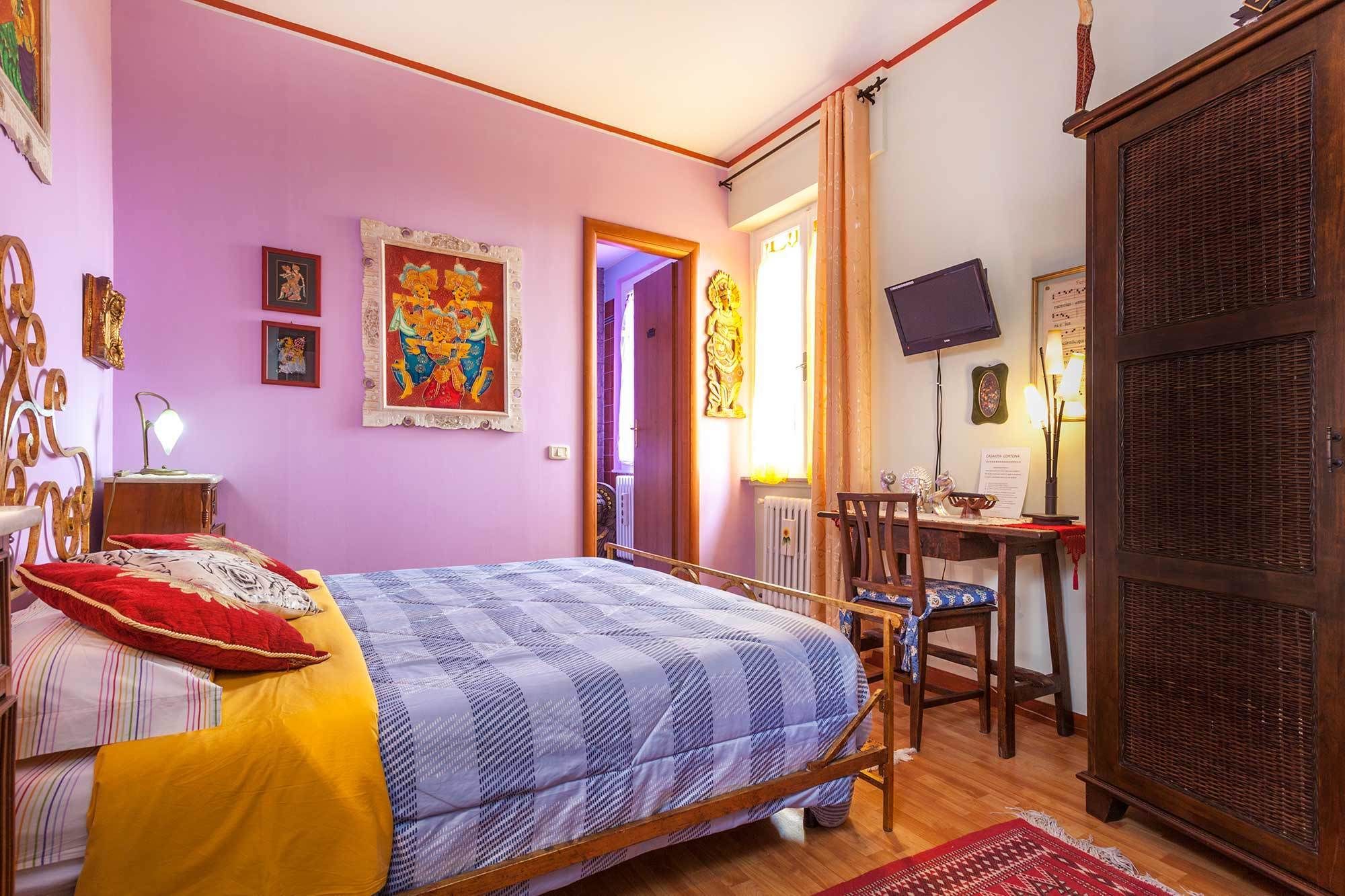 A bedroom with a bed, a desk, a chair, and a TV.